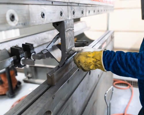 Closeup of operator's gloved hand removing bent metal plate from a press brake.